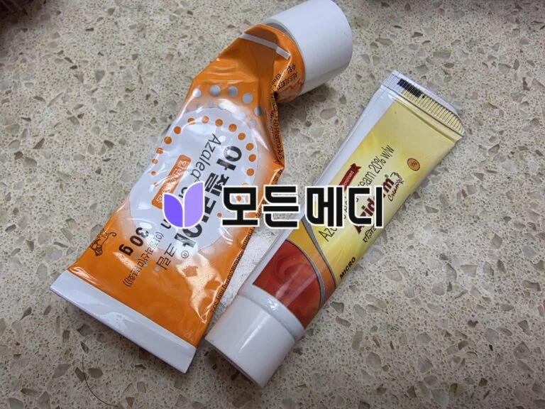 Two toothpaste tubes, one orange-and-white with Korean text, and a yellow-labeled tube, lay diagonally on a speckled countertop.