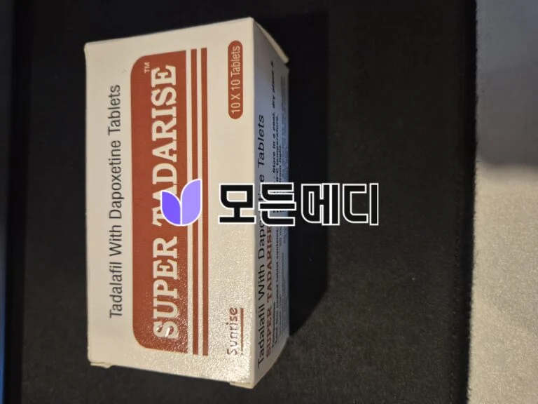 Box of tablets on a dark surface; white packaging with a red-brown panel saying '10 x 10 Tablets' and a purple leaf-like logo, oriented diagonally to the left.