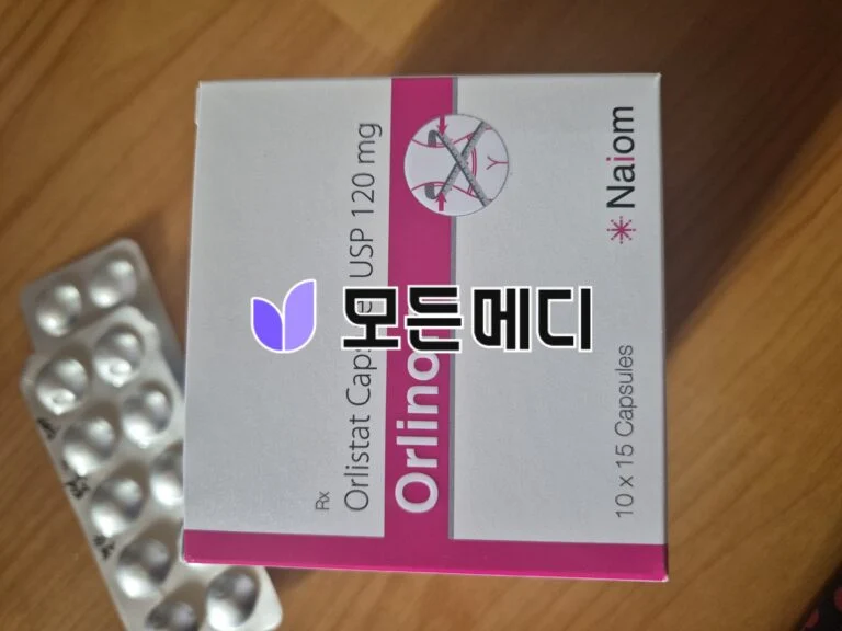 Box of orlistat 120 mg weight‑loss capsules with a blister pack of white pills nearby on a wooden surface, pink and white packaging visible.
