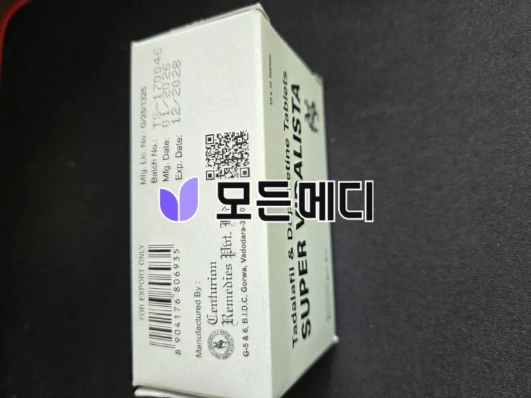 White rectangular medicine box angled on a dark surface, showing a barcode, printed text, a QR code, and a small purple logo partially visible on the side.