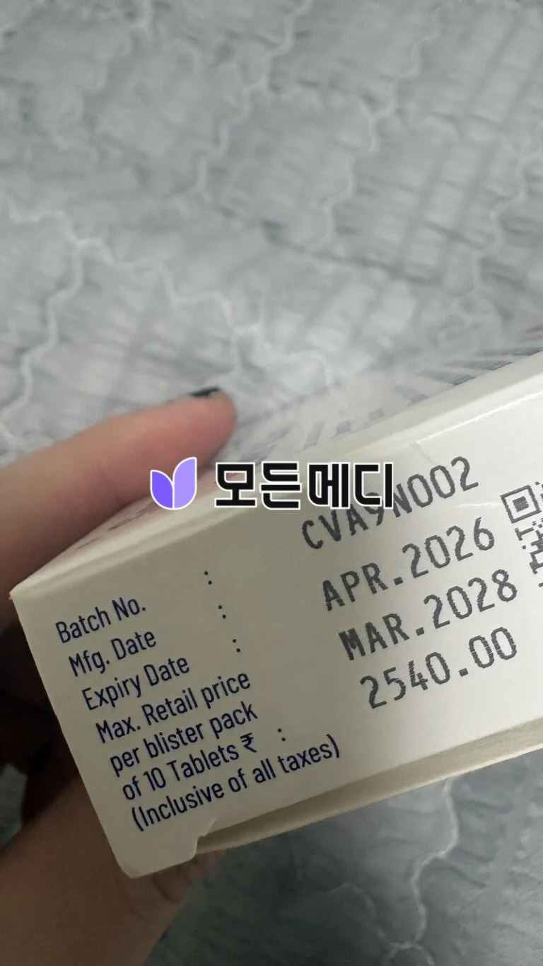 Close-up of a medicine box label being held, showing batch number, manufacturing/expiry dates, and a purple leaf logo with Korean text.