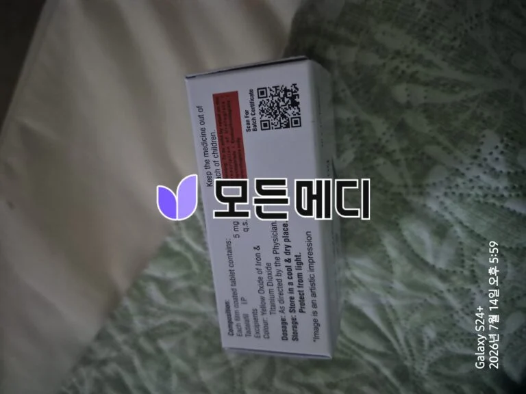Close-up of a medicine box with a red warning label and a QR code on the side, resting on fabric.