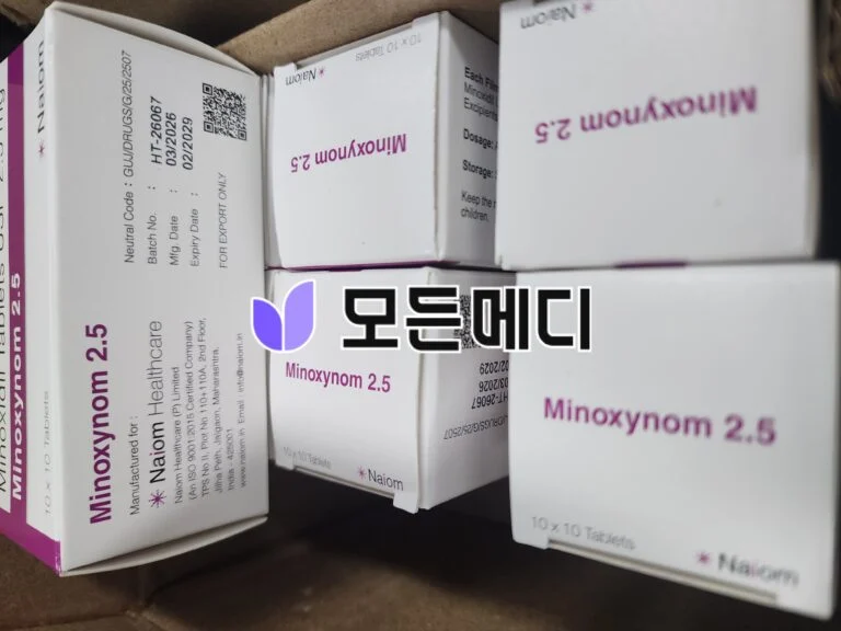 White medicine boxes labeled Minoxynom 2.5 with purple logos, stacked in a cardboard box.