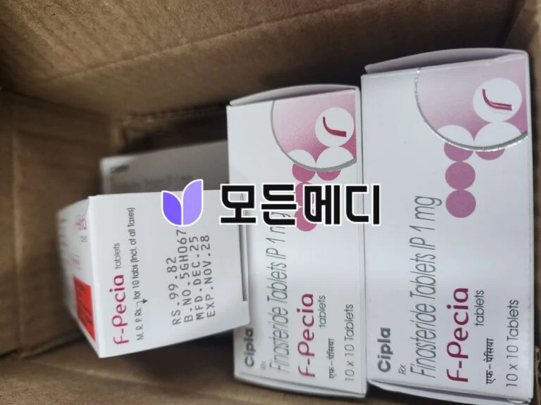Boxes of medication packaging inside a cardboard box, white with pink circular logo and pink text on the sides (pharmaceutical packaging).