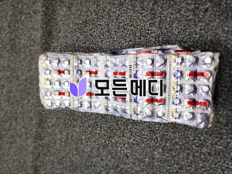 Blister packs with white and colored pills lying on a gray carpeted floor, viewed from above.