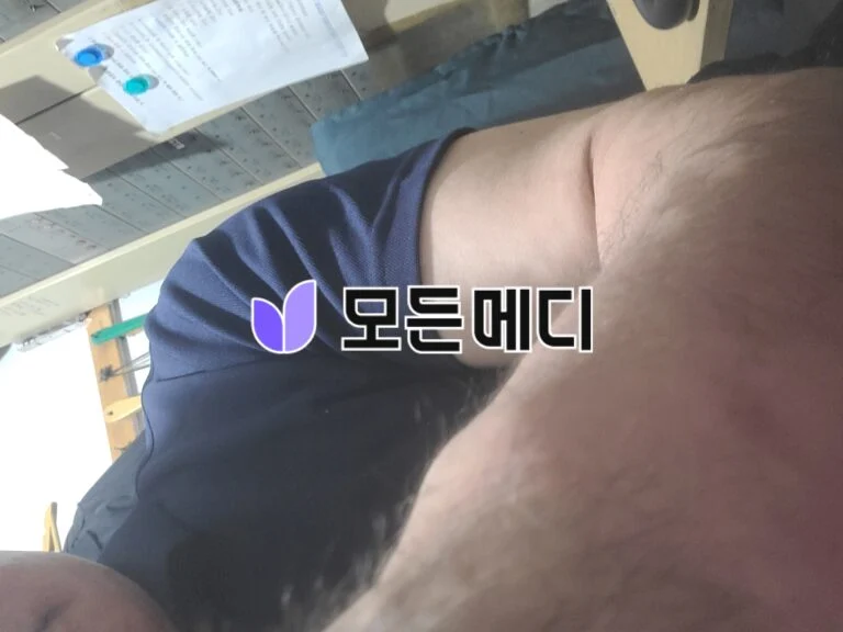 Close-up of a person's forearm in a dark blue shirt, with a purple logo and Korean text overlay, in a classroom or office setting.