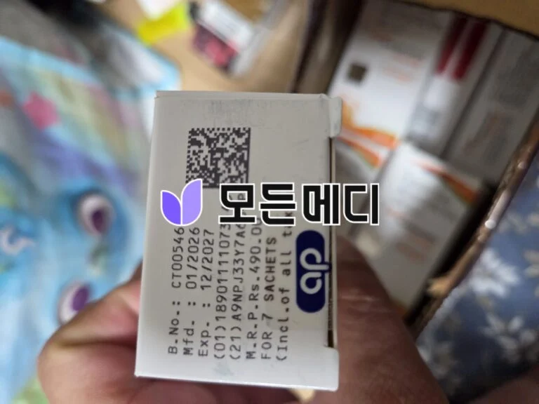 Close-up of a white box with a small QR code and a purple butterfly logo, held near a blurred store shelf.