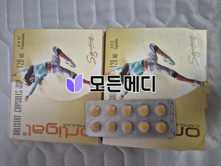 Two beige capsule boxes with two blister packs of orange pills on a quilted surface.